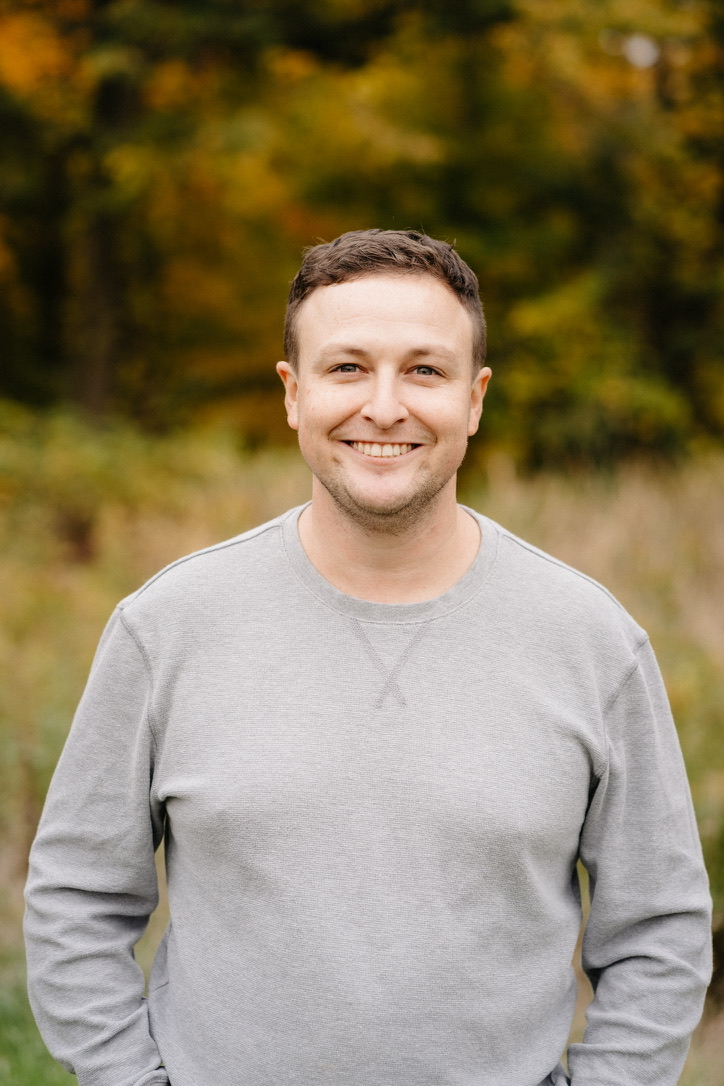 Nathaniel Arfin smiling outdoors in his recent grey-sweater photograph